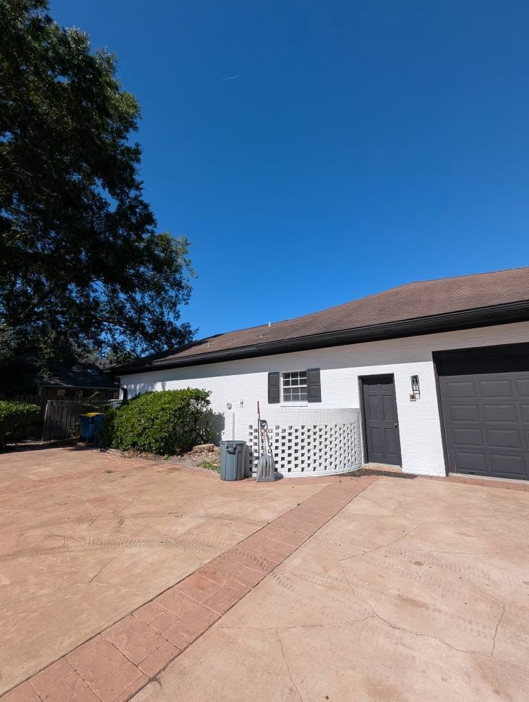 The same white brick home after the dead tree was removed, with a clear driveway and open blue sky