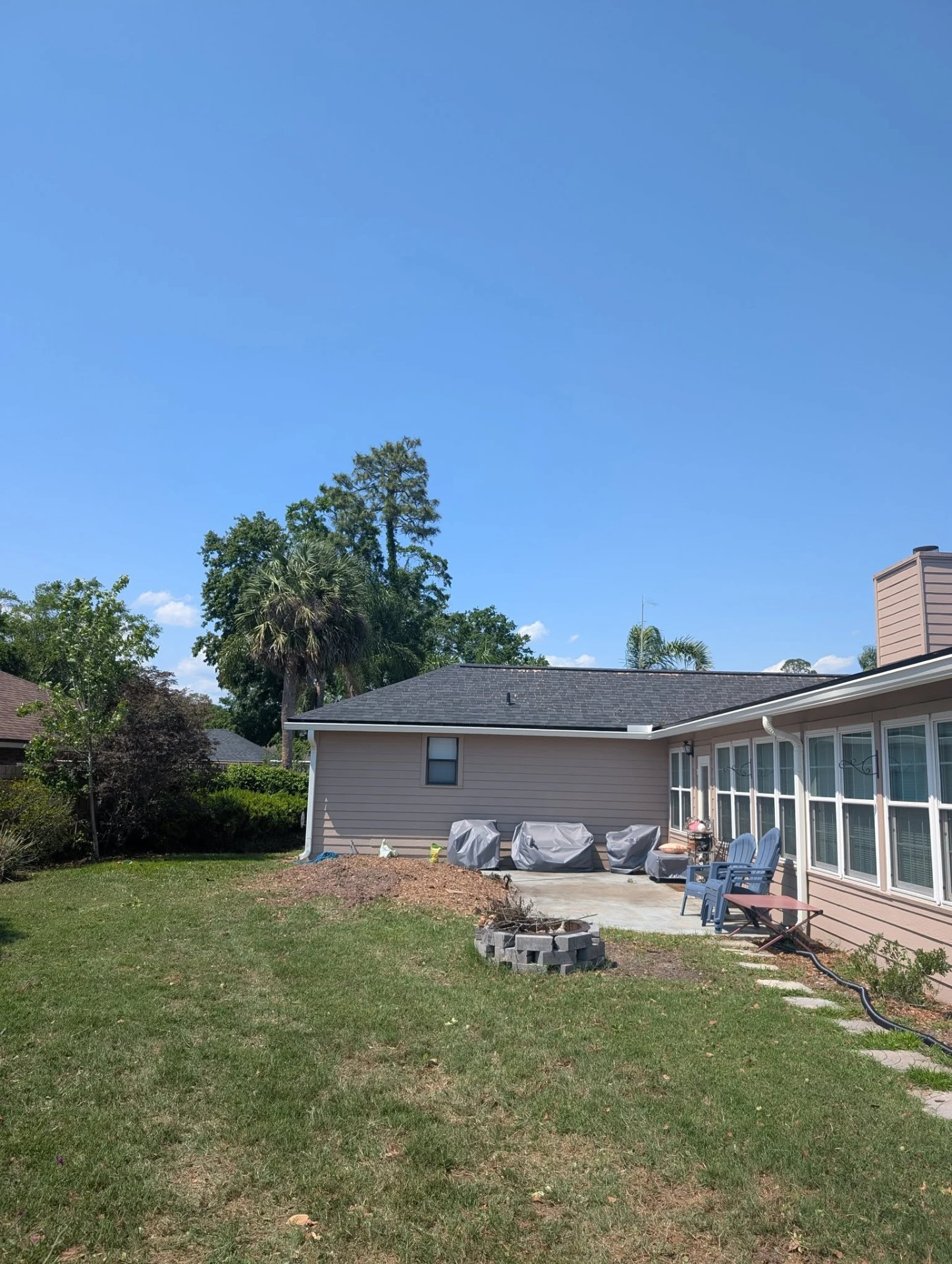The same backyard patio after the hardwood was removed, with open blue sky and stump mulch along the wall