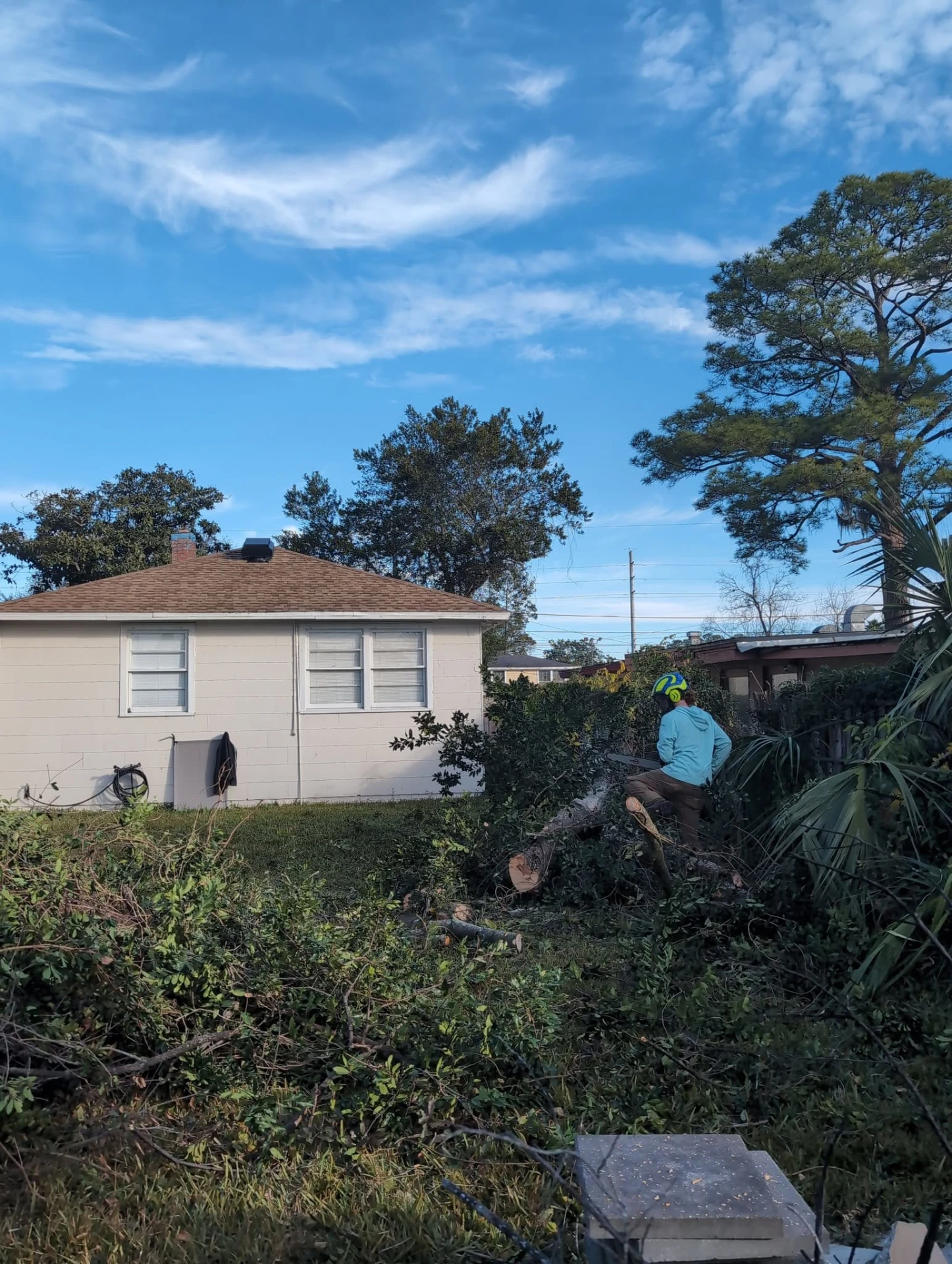 Crew member in a helmet bucking a downed tree into rounds in a backyard after a failure